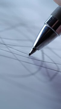 A vertical, extreme close-up of a metallic pen tip drawing intricate, chaotic lines on a piece of white paper.
