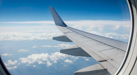 Fototapeta premium Airplane Window View with the Wing Flying Above the Clouds and Blue Sky