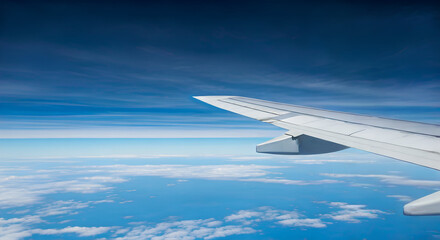 Fototapeta premium Airplane Window View. Wing Flying Above Soft Clouds and Clear Blue Sky