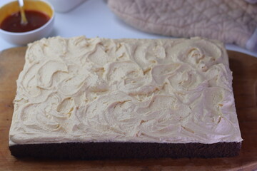 Chocolate sheet cake with a thick layer of buttercream frosting placed on a wooden cutting board