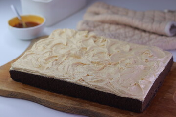 Chocolate sheet cake with a thick layer of buttercream frosting placed on a wooden cutting board