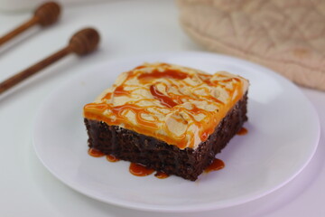 Moist chocolate cake slice topped with buttercream frosting and drizzled with caramel cream sauce.