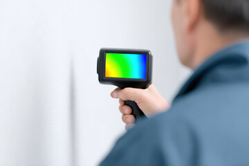 Thermal camera inspection by technician detecting temperature variations on white wall with colorful heat map display