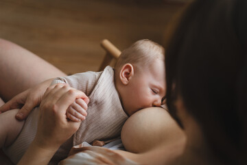 A mother sits in a wooden chair, gently breastfeeding her baby in a warm and softly lit room. Sunlight filters through the curtains, creating a peaceful atmosphere.
