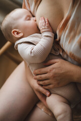 A mother sits in a wooden chair, gently breastfeeding her baby in a warm and softly lit room. Sunlight filters through the curtains, creating a peaceful atmosphere.