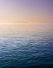 Fototapeta premium Serene Ocean Vista at Dawn with Distant Island Silhouette and Soft Pastel Sky Hues Reflecting on Calm Waters