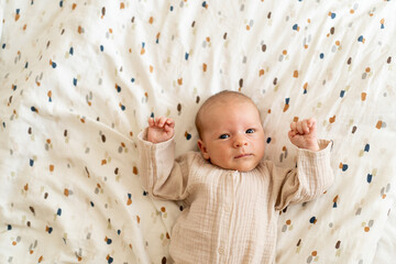 A newborn baby, lying on a soft, colorful blanket, gazes curiously at the viewer with wide eyes. The warm atmosphere highlights the baby's gentle features and innocence.