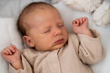 A newborn baby, lying on a soft, colorful blanket, gazes curiously at the viewer with wide eyes. The warm atmosphere highlights the baby's gentle features and innocence.