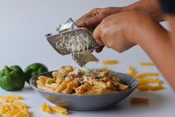 Hand grating cheese over creamy white sauce rigatoni pasta