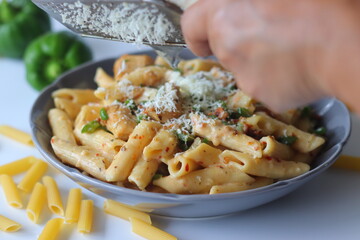 Hand grating cheese over creamy white sauce rigatoni pasta