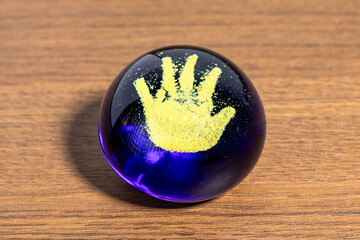 A vibrant yellow handprint is strikingly embedded within a smooth, dark blue glass paperweight, resting on a polished wooden surface, a unique artistic piece.