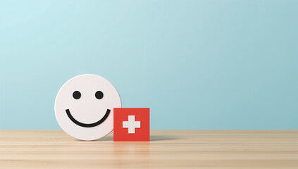 Smiley face next to red health cross on wood surface representing medical care, positivity, and patient wellness.