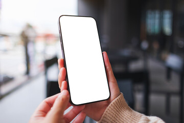 Mockup image of a woman holding and using mobile phone with blank desktop screen in cafe
