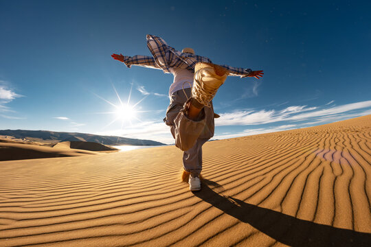 Happy young woman girl tourist is having fun and runs at desert sunset against blue sky and sand dune