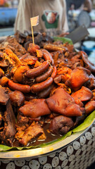 a large platter piled with richly braised pork dishes, including sausages, trotters, and chunks of tender meat in dark savory sauce, displayed on a banana leaf at a food stall. pork food festival