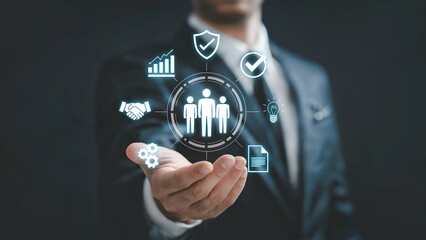 A businessman in a suit holding out a hand with glowing digital overlays showing teamwork icons analytics security and innovation in a dark workspace