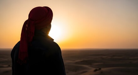 Silhouette of a person in a red turban from behind, watching the golden sun set over a vast desert landscape.