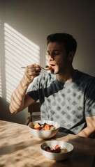 Young man enjoying a healthy fruit salad for breakfast in sunlit room.
