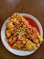 Delicious and crispy fuyunghai, a classic Chinese omelet dish, served on a white plate with vibrant sweet and sour sauce and green peas, ready to be enjoyed as a hearty meal