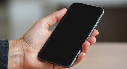 Hand Holding Black Smartphone with Blank Screen in Indoor Setting for Technology Showcase