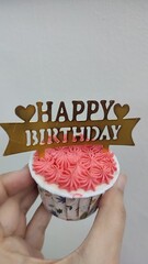 A picture of hands holding a cupcake with birthday decoration cream.