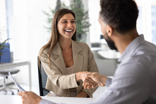 Happy young Hispanic businesswoman shaking hands with male African coworker