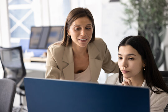 Two positive diverse female coworkers looking at computer monitor together