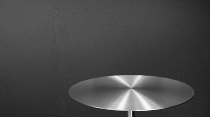 A circular, brushed stainless steel or chrome tabletop with radial reflections, positioned against a rough, speckled black concrete or stucco background, ideal for product display mockup.