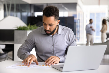 Fototapeta premium Focused young African product manager man analyzing paper sales reports