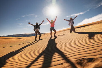 Group of three happy young women are standing in winner poses with open arms in desert dunes against blue sky and sun © cppzone
