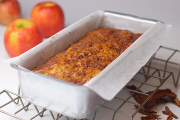 Freshly baked apple cinnamon bread loaf in a parchment lined metal pan on a cooling rack