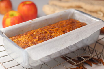 Freshly baked apple cinnamon bread loaf in a parchment lined metal pan on a cooling rack
