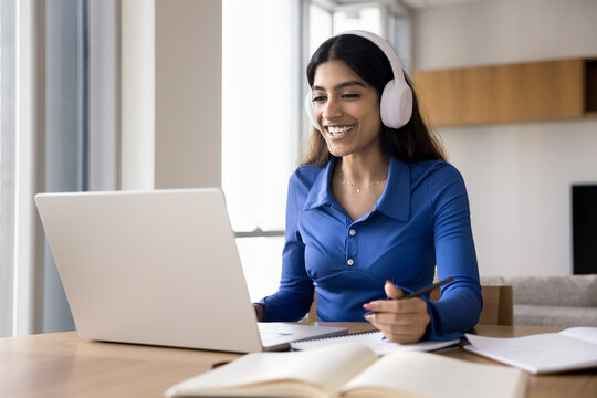 Cheerful student girl in wireless headphones watching learning webinar