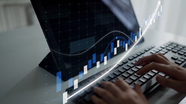 Focused hands typing on a keyboard while analyzing a digital stock market chart displayed on a computer screen, representing financial growth and modern business analysis. Copula