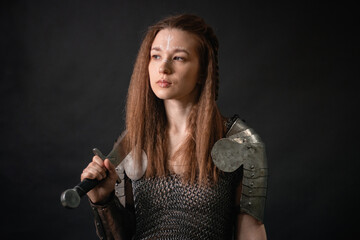 Naklejka premium Portrait of a young woman, fantasy warrior in armor with a sword in her hands isolated on a dark background