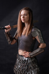 Naklejka premium Portrait of a young woman, fantasy warrior in armor with a sword in her hands isolated on a dark background
