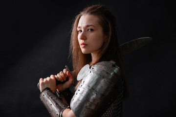 Naklejka premium Portrait of a young woman, fantasy warrior in armor with a sword in her hands isolated on a dark background