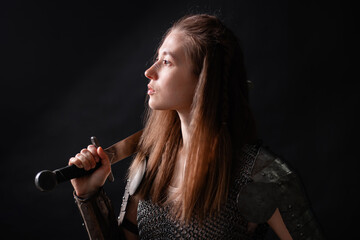 Naklejka premium Portrait of a young woman, fantasy warrior in armor with a sword in her hands isolated on a dark background