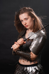 Naklejka premium Portrait of a young woman, fantasy warrior in armor with a sword in her hands isolated on a dark background
