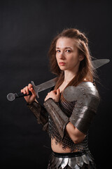 Naklejka premium Portrait of a young woman, fantasy warrior in armor with a sword in her hands isolated on a dark background