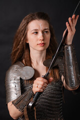 Naklejka premium Portrait of a young woman, fantasy warrior in armor with a sword in her hands isolated on a dark background