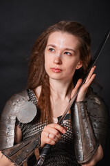Naklejka premium Portrait of a young woman, fantasy warrior in armor with a sword in her hands isolated on a dark background