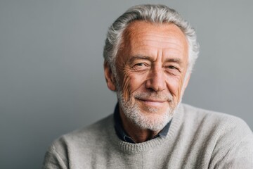 Smiling senior man with grey hair wearing a light sweater against a grey background showcasing warmth and friendliness in a modern portrait style