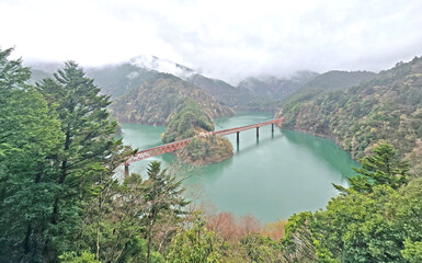 Scenic view of a red bridge over a lake surrounded by lush green mountains