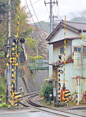 A railway crossing signal stands tall, warning of an approaching train in a rural Japanese setting