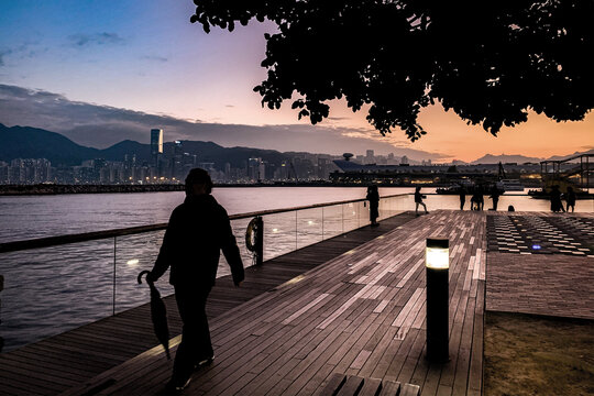 Silhouette of a person walking on a waterfront boardwalk at dusk in Hong Kong