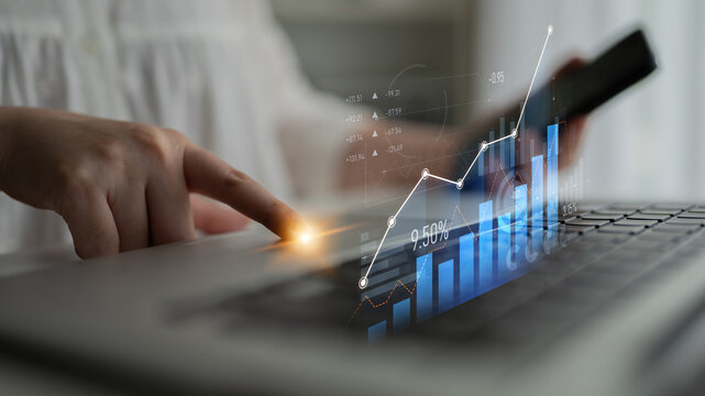 A businesswoman interacts with her smartphone while analyzing financial data and statistics on her laptop, showcasing modern technology in the workplace. Scalp - Powered by Adobe