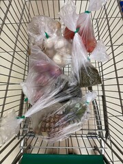 A top-down view of a supermarket shopping cart filled with fresh produce packed in plastic bags for grocery retail. © Yunqi