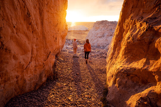 Two girls tourists are standing at lake shore or beach near the gorge and enjoys beautiful sunset view