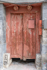 Full frame close up of an old weathered red wooden door in China with peeling paint exposed wood texture and decorative metal studs